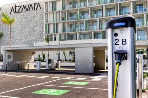 Un estacionamiento con estaciones de carga para vehículos eléctricos, un edificio de fachada moderna y un cielo despejado.