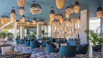 A modern lounge area with wicker pendant lighting, blue upholstered chairs, and a patterned floor.