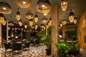 A lobby with multiple seating areas, large potted plants, and hanging wicker chandeliers. - Atzavara Hotel Spa (Santa Susanna)