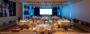 A conference room with multiple round tables set for a meeting, equipped with chairs, tables, and a large screen at the front.