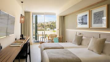 A hotel room with two beds, a desk with a chair, a table with chairs, and a view of the city.