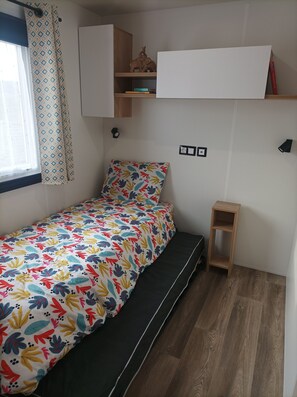 A small, neatly arranged bedroom with a single bed, a small wooden shelf, and a wall-mounted cabinet.