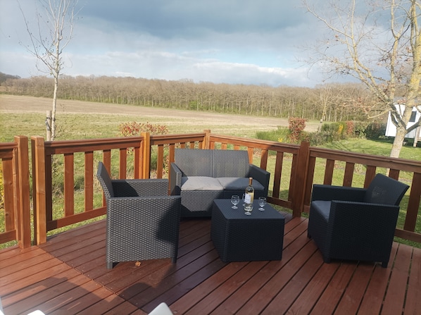 A wooden deck with wicker furniture and a bottle of wine.