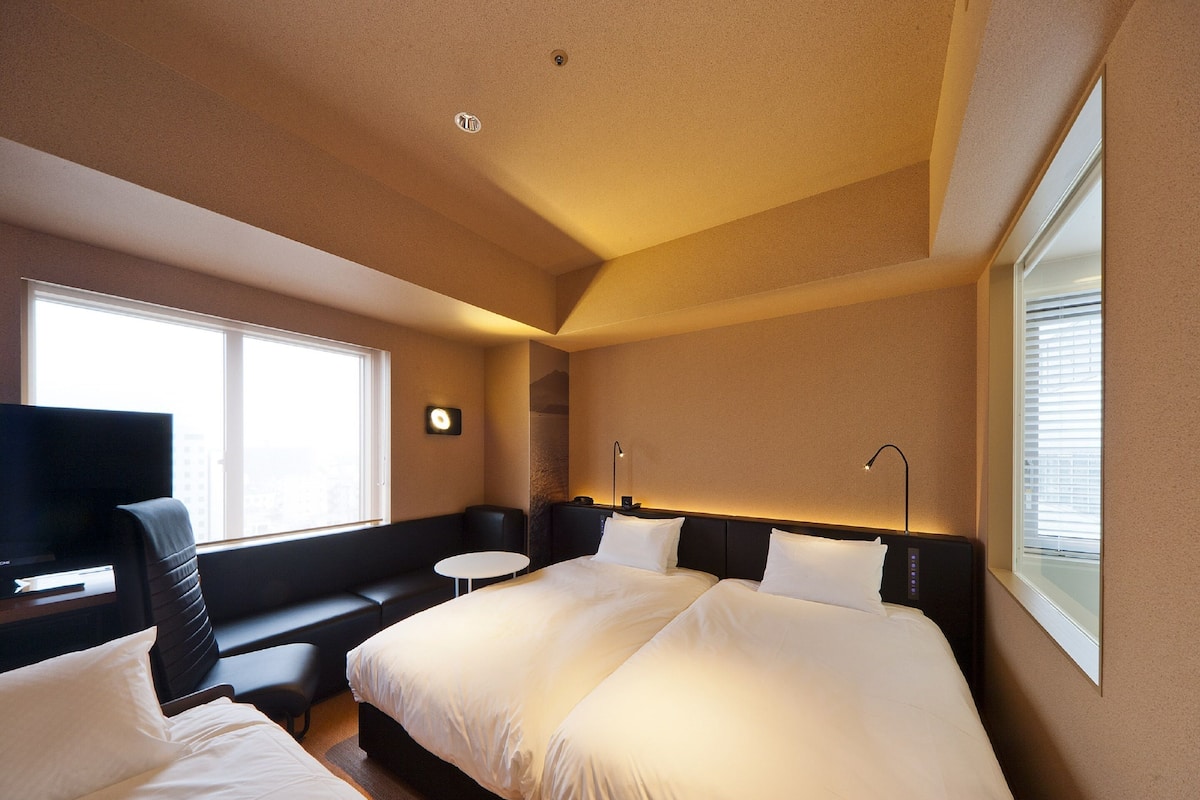 A hotel room with two beds, a sofa, a TV, and a small table.