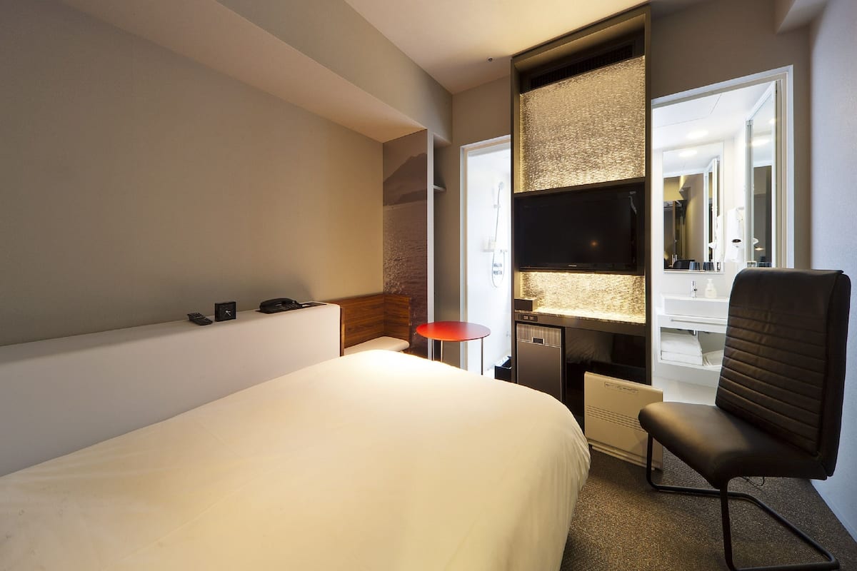 A hotel room with a large bed, a desk with a chair, a television, and a bathroom visible through an open door.