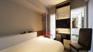 A hotel room with a large bed, a desk with a chair, a television, and a bathroom visible through an open door.