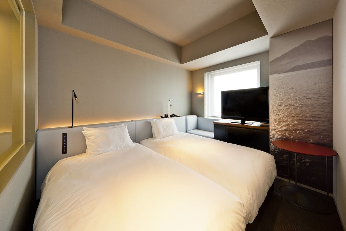 A hotel room with a large bed, a desk with a TV, and a window with a mountain view.