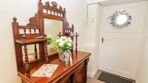 Une console en bois, surmontée d’un miroir, agrémentée d’un vase de fleurs blanches et d’un livre à motifs floraux.