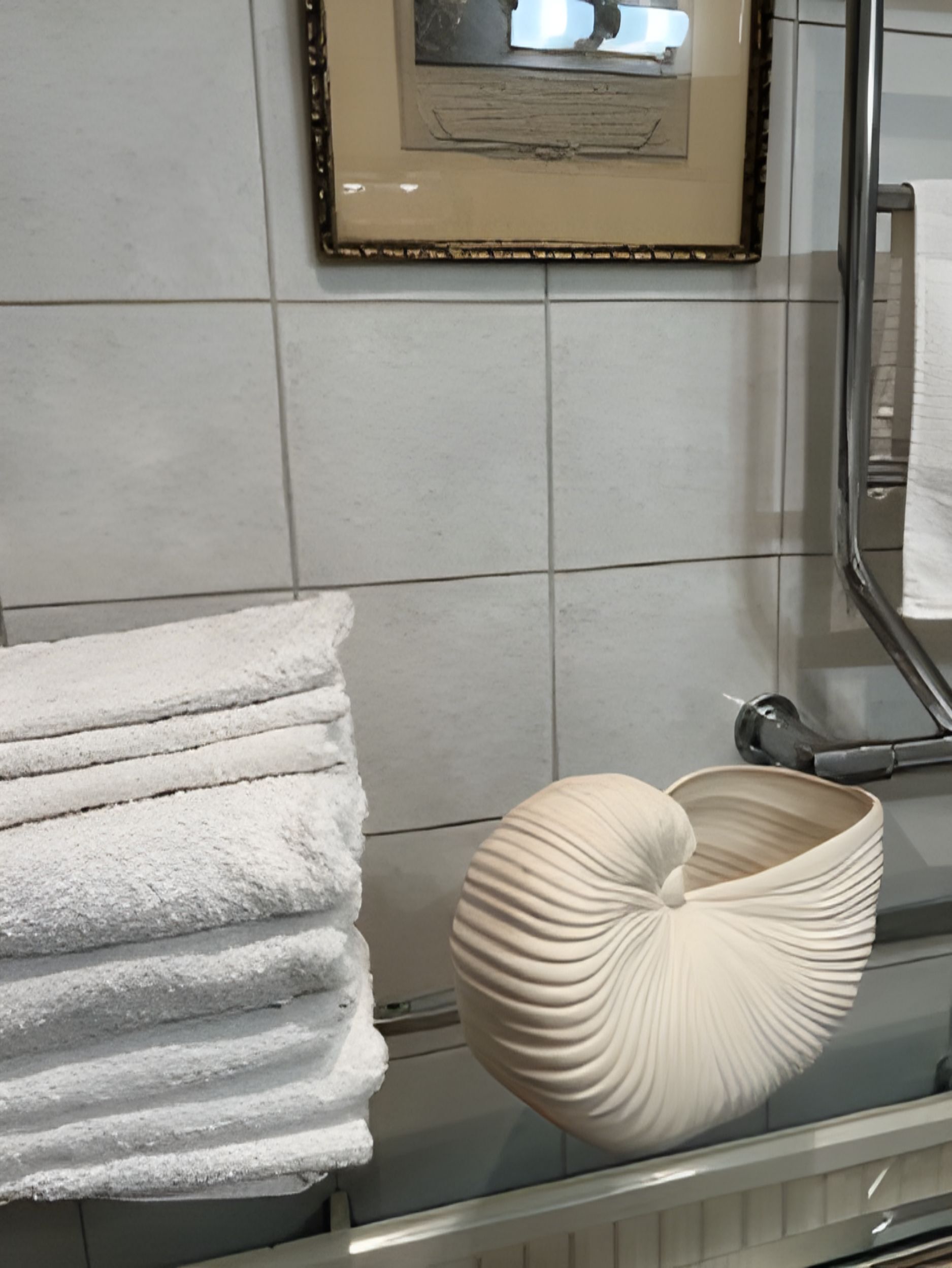 Ein Badezimmer mit gefliesten Wänden, einem gerahmten Bild, einem Handtuchhalter mit gefalteten Handtüchern und einer dekorativen Schale.
