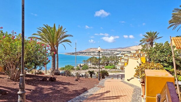 A coastal view with a paved walkway, palm trees, and a clear blue sky. - House CASA MAJA Costa Calma Oceanview Garden WiFi (Costa Calma)