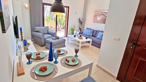 A dining area with a table set for four, a sofa, and a TV in the background. - House CASA MAJA Costa Calma Oceanview Garden WiFi (Costa Calma)
