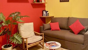 A living room with a brown sofa, red cushions, a wooden chair, a potted plant, and shelves with books and decorative items. - The Patio near Bergamo with a summer pool (Mozzo)