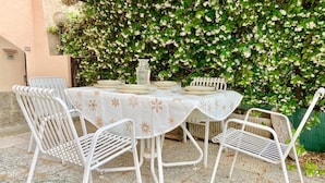 A table set outdoors with a white tablecloth, surrounded by white metal chairs, against a backdrop of flowering bushes. - The Patio near Bergamo with a summer pool (Mozzo)