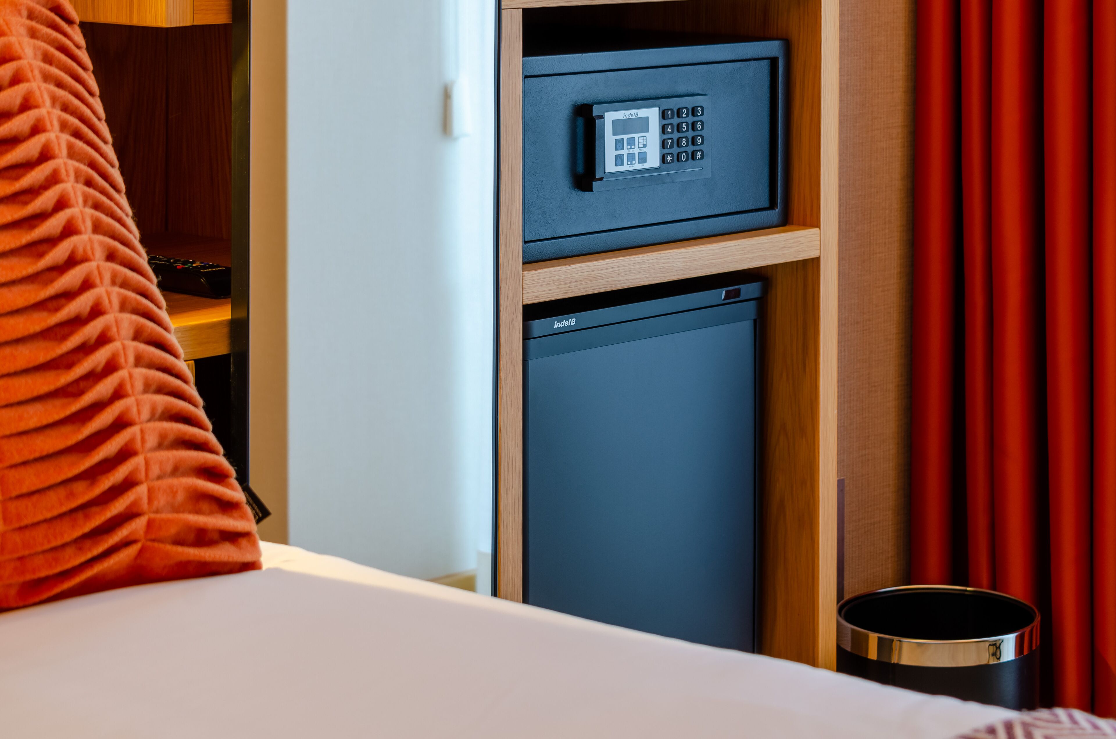 A hotel room with a minibar, a small refrigerator, and a bed with an orange pillow.