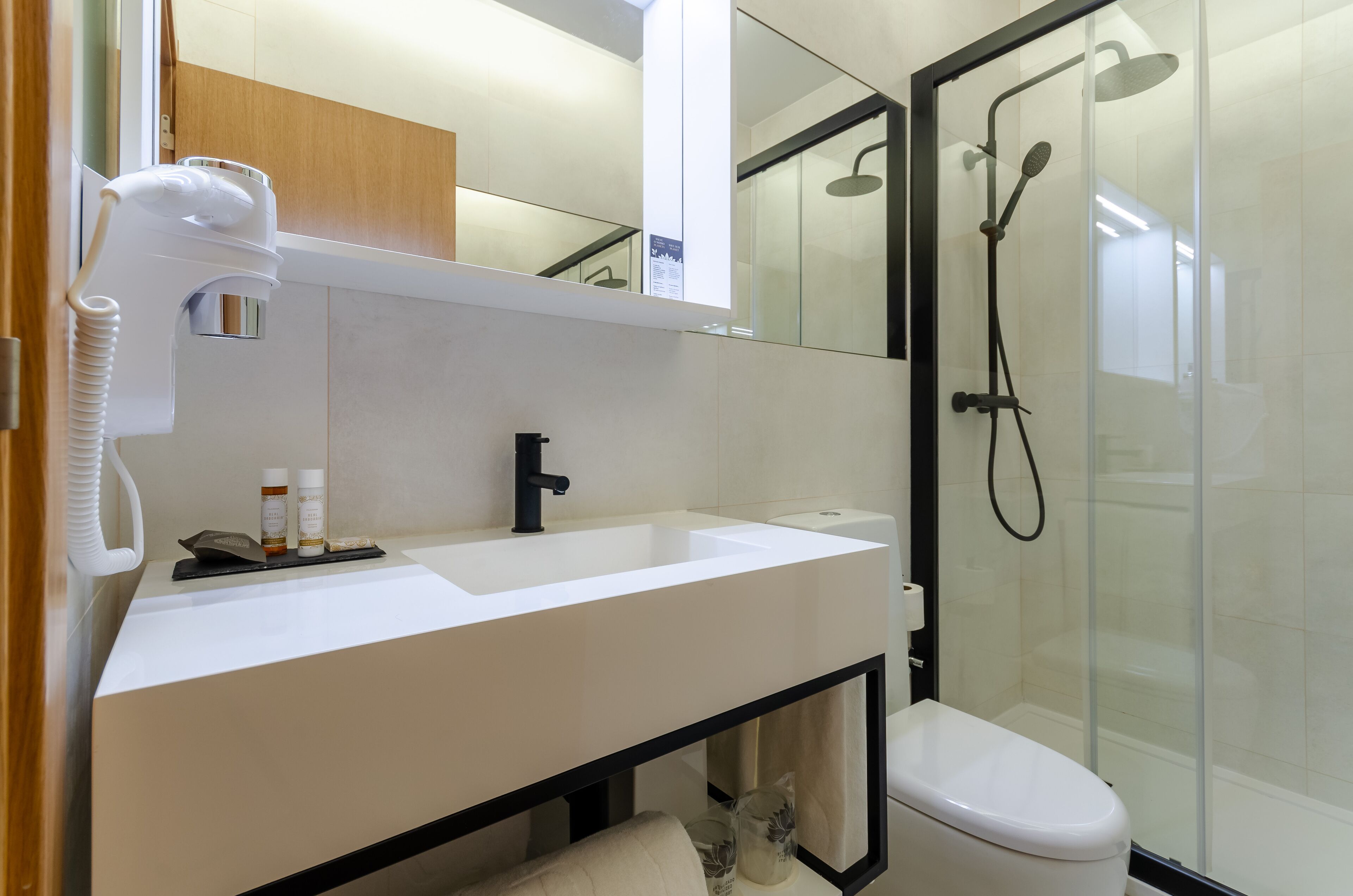 A modern bathroom with a white sink, a black faucet, a glass shower enclosure, and a white toilet.
