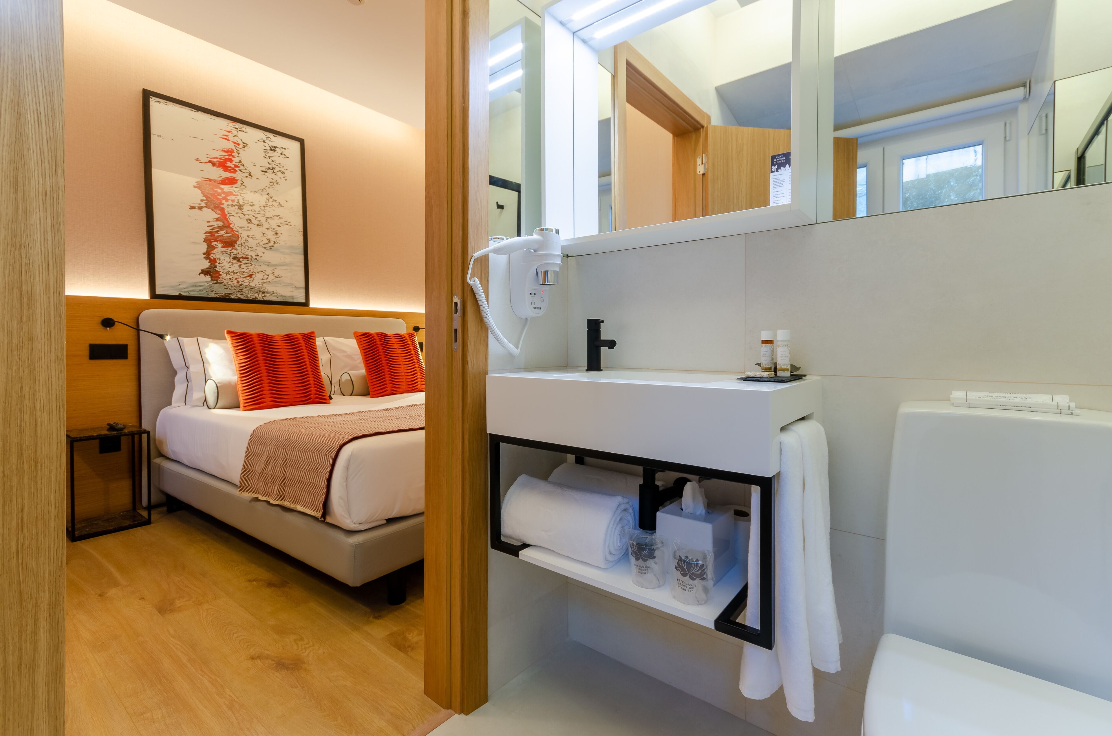 A modern hotel room with a bed, a vanity with toiletries, a towel rack, and a large mirror.