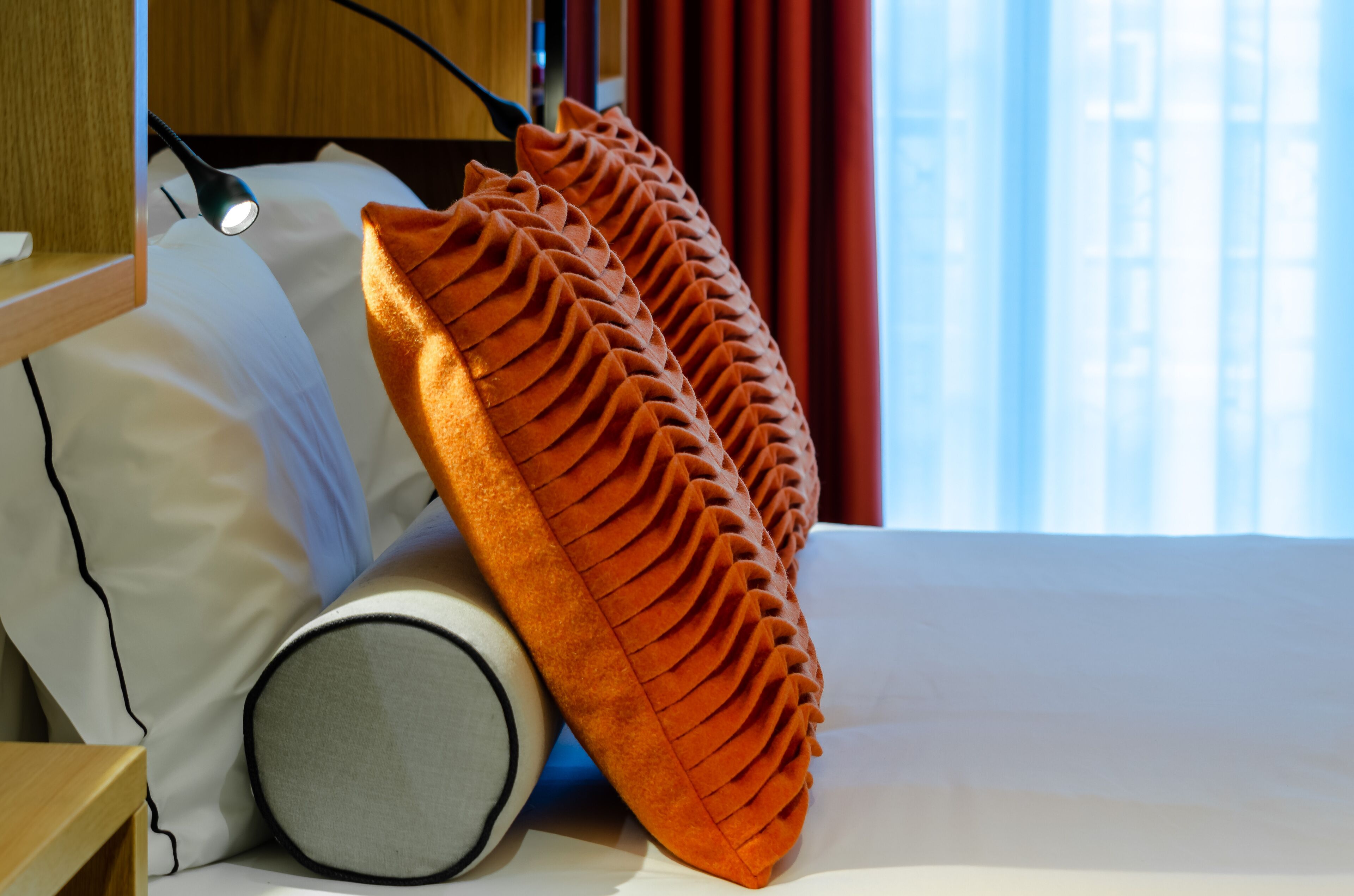A neatly made bed with a white pillow, a round pillow, and a textured orange pillow.
