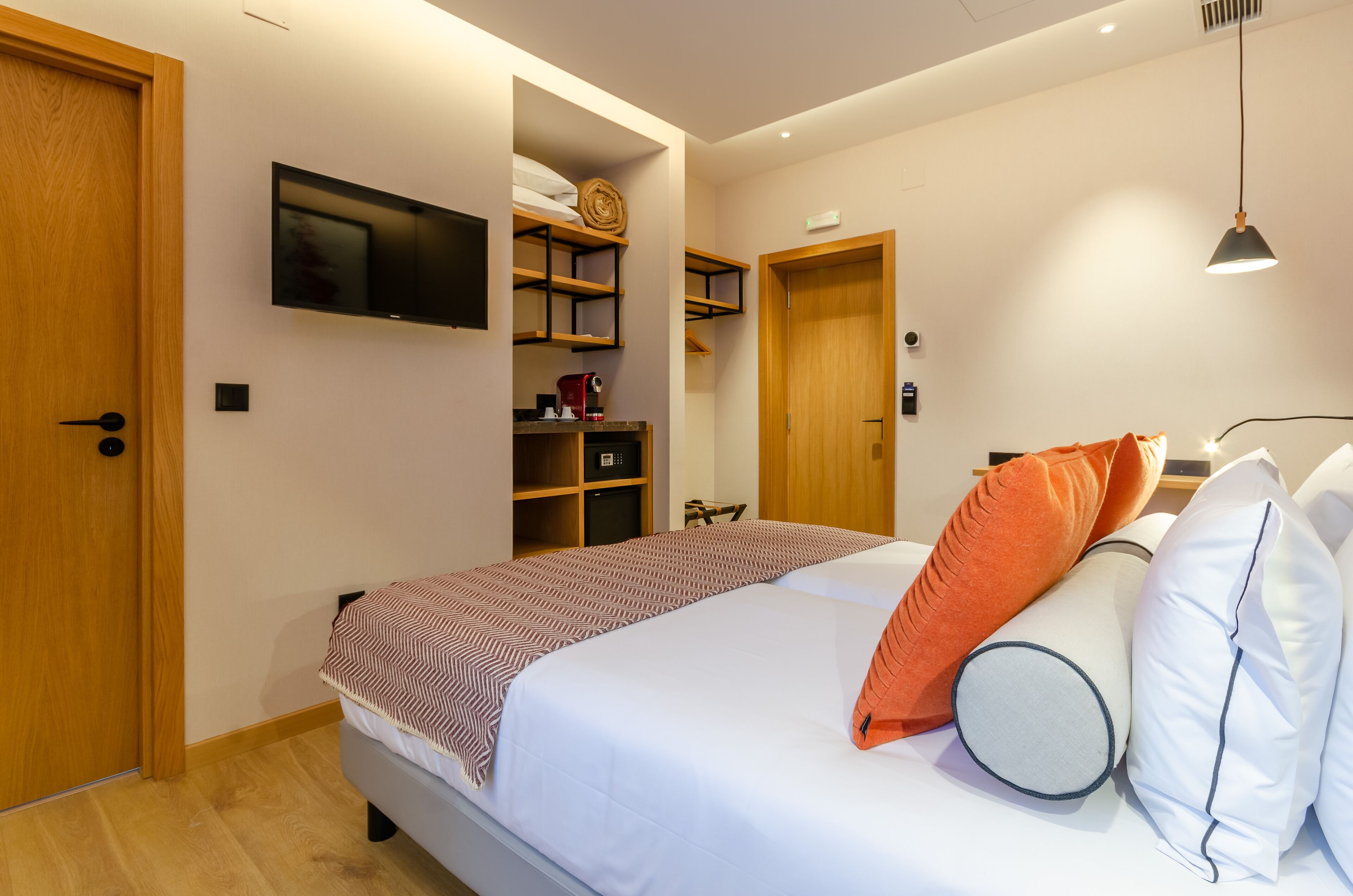 A bedroom with a bed, a TV mounted on the wall, a wooden door, and a shelf with items.
