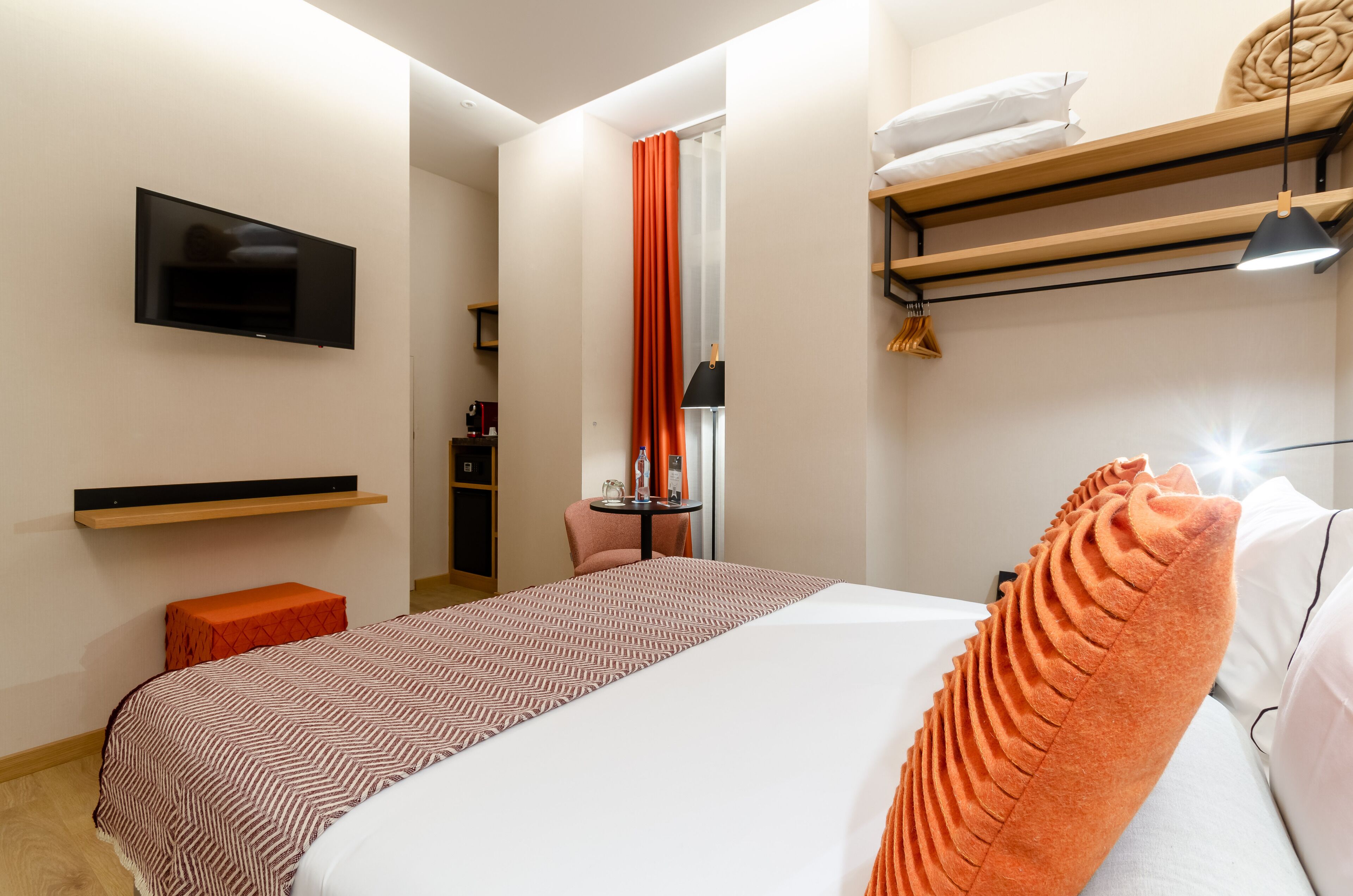 A hotel room with a bed, a TV mounted on the wall, a small table, and a chair.