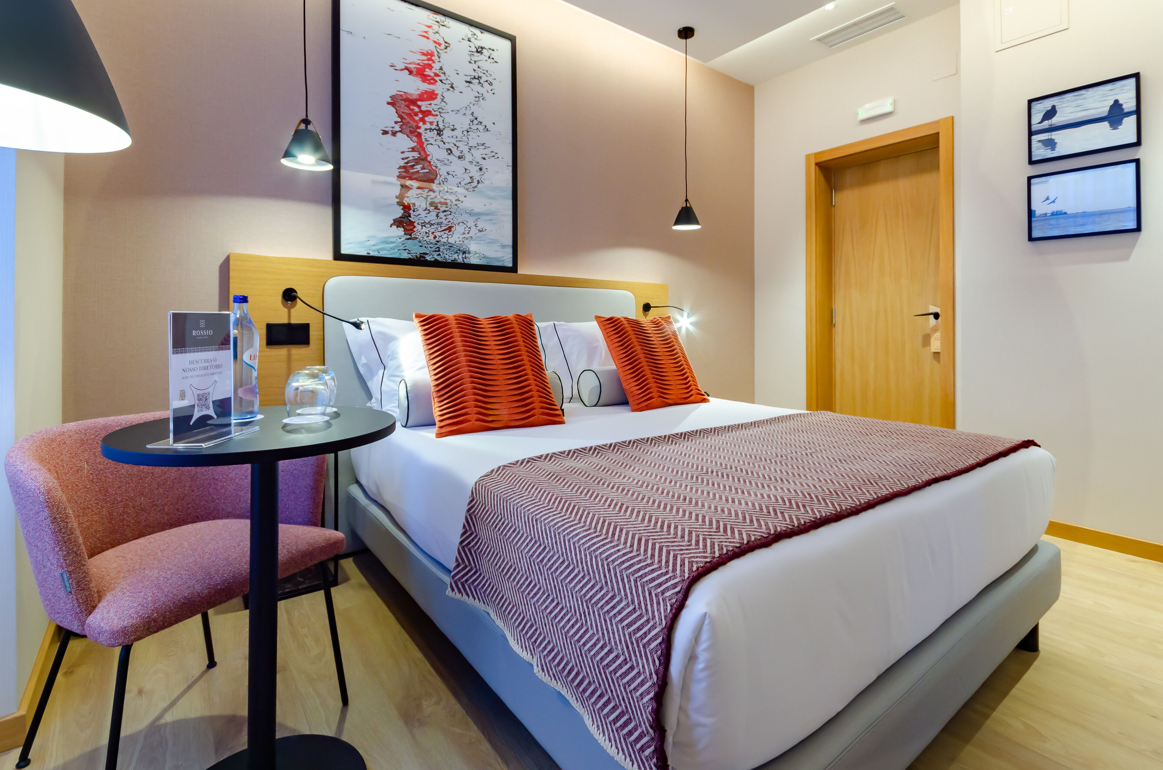 Une chambre d’hôtel avec un lit, une table ronde et une chaise, une bouteille d’eau, un verre et un panneau.