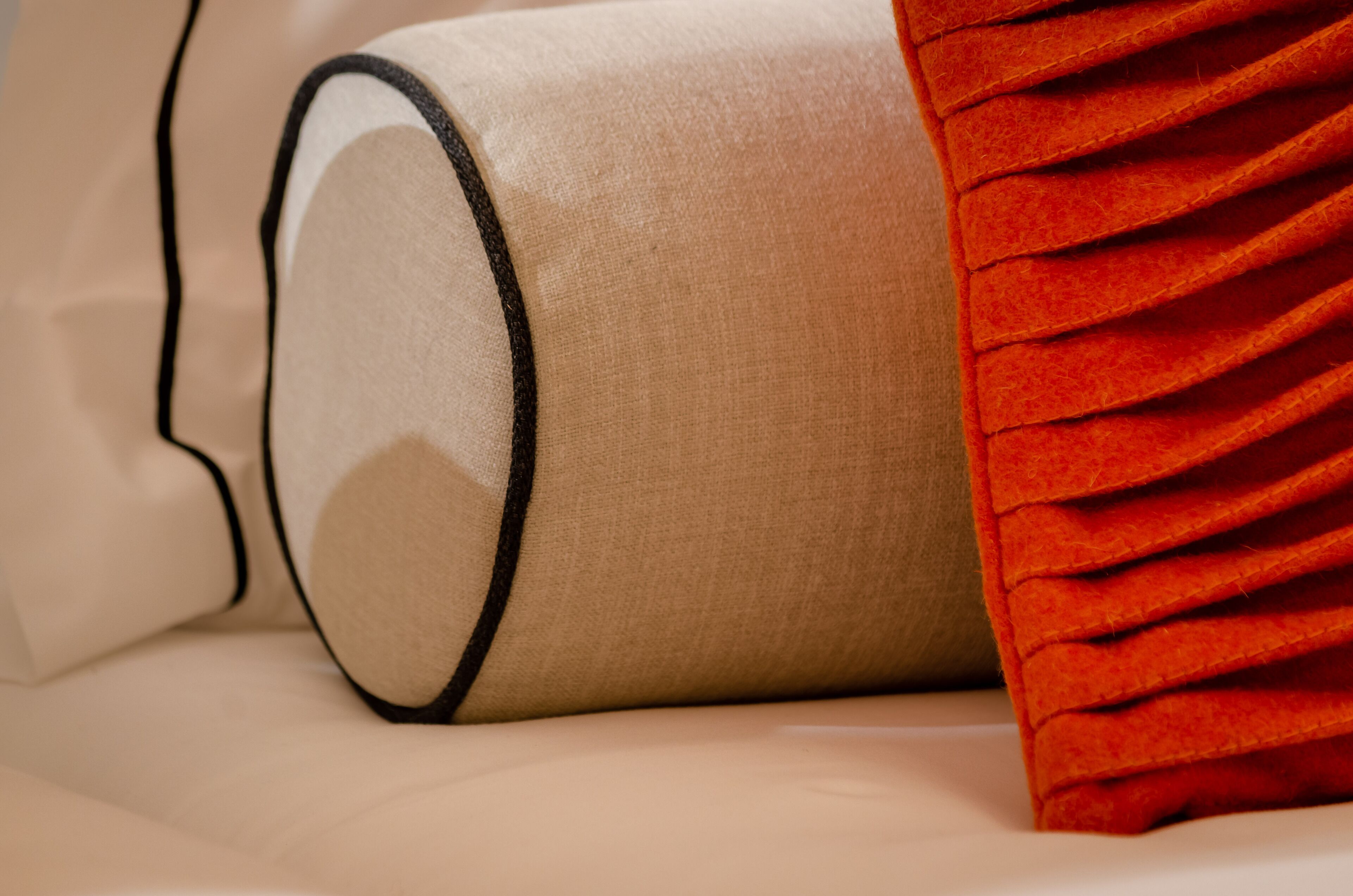 Un lit avec un oreiller beige et un oreiller rouge à bords frangés.