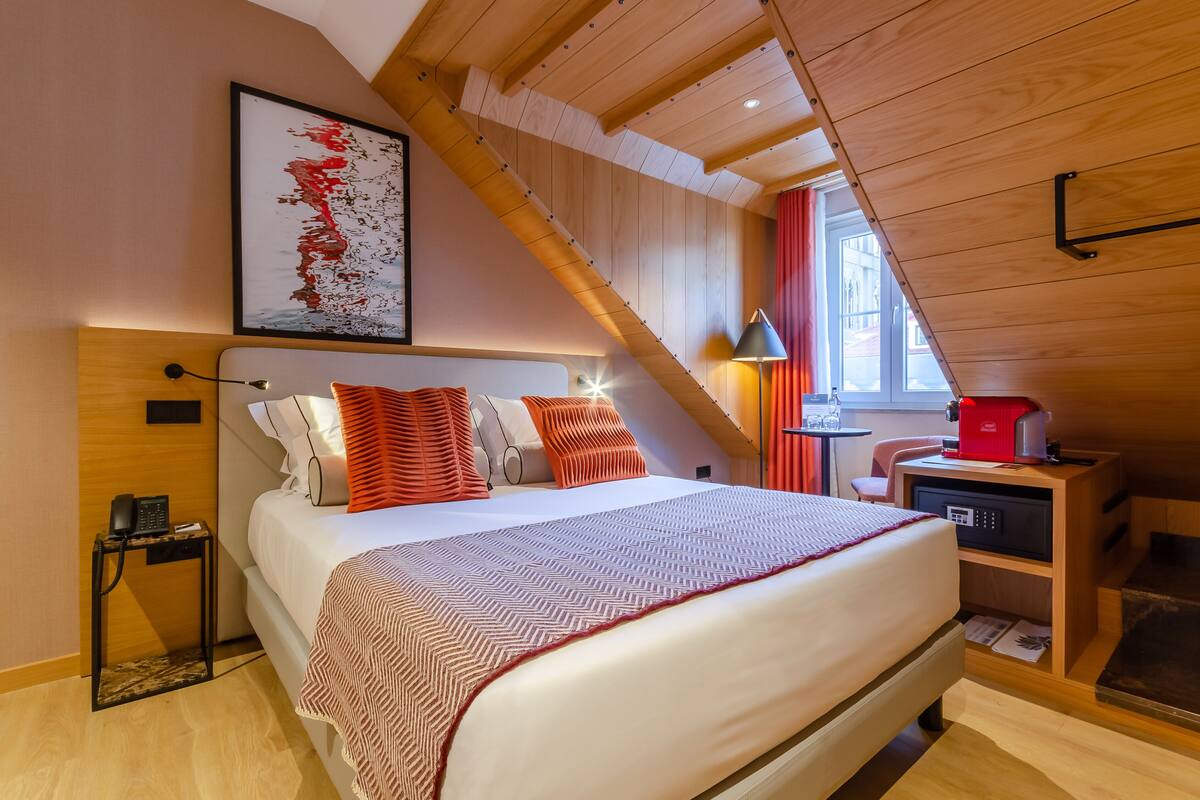 A bedroom with a bed, a nightstand, a lamp, a coffee machine, and a window.