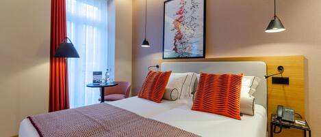 Habitación de hotel con una cama grande, un escritorio con teléfono y una ventana con cortinas rojas.