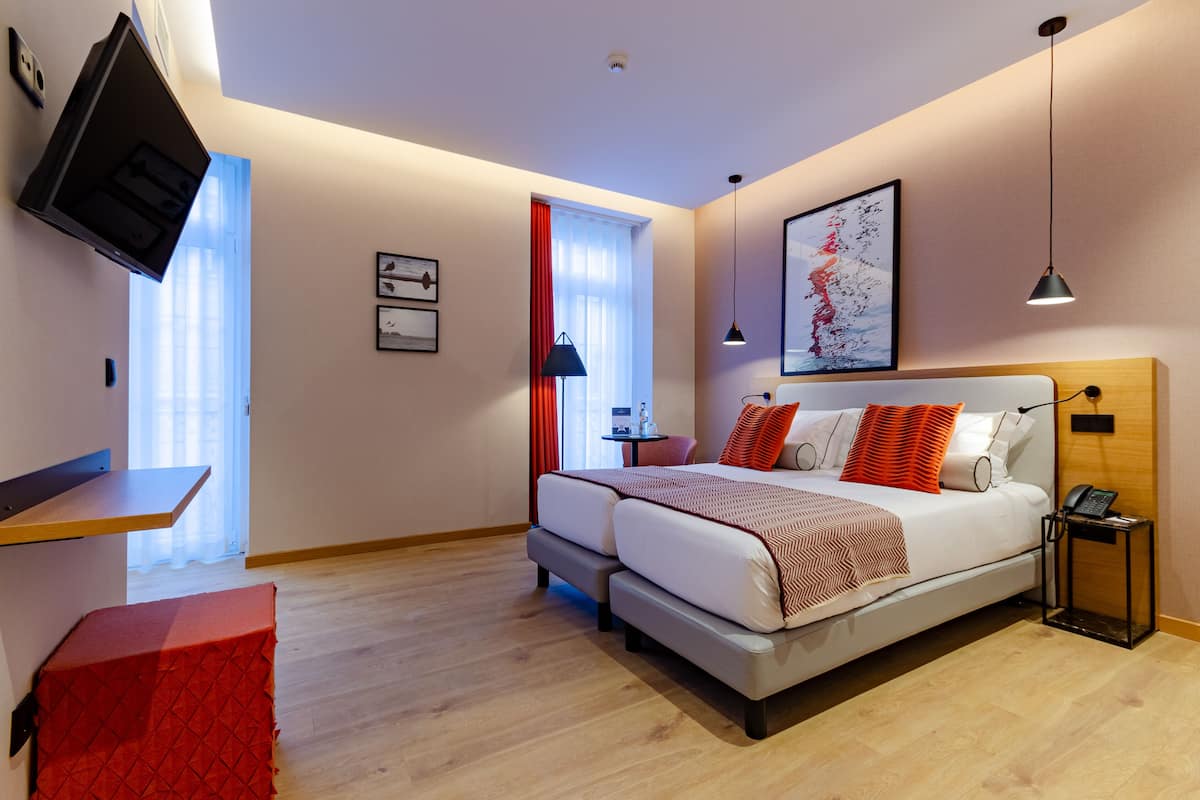A modern hotel room with a bed, a desk, a TV, and a window with curtains.