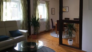 A living room with a sofa, a glass coffee table, and potted plants. There is a dining area with a table and chairs.