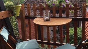 A wooden deck with a round table and two chairs, surrounded by a wooden fence with potted plants.