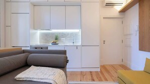 A modern kitchen with white cabinets, a built-in stove, and a small island with a plant and fruit bowl.