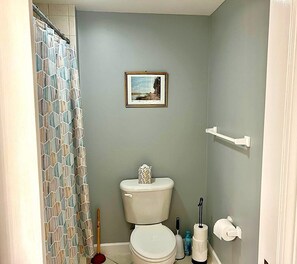 A small bathroom with a toilet, a shower curtain, a picture on the wall, and a toilet paper holder. - XPLORIE ACTIVITIES & LINENS INCLUDED*!  Close to shopping, restaurants, community center, park & more! (Ocean City)
