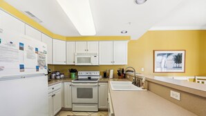 Eine Küche mit weißen Schränken, einer Mikrowelle, einem Backofen, einer Spüle und einer Arbeitsfläche mit diversen Gegenständen.