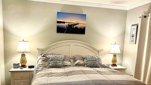 Ein Schlafzimmer mit einem Bett, zwei Nachttischen mit Lampen, einem Beistelltisch mit einer Uhr und einem gerahmten Bild an der Wand.
