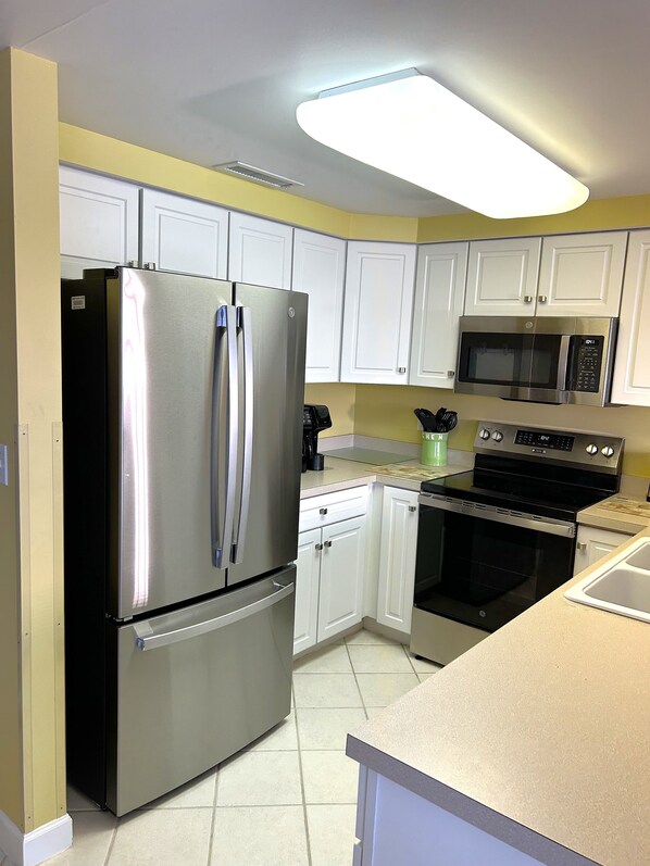 A modern kitchen with white cabinets, stainless steel appliances, and a tiled floor. - XPLORIE ACTIVITIES & LINENS INCLUDED*!  Close to shopping, restaurants, community center, park & more! (Ocean City)