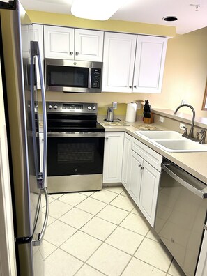 A kitchen with white cabinets, stainless steel appliances, and a tiled floor. - XPLORIE ACTIVITIES & LINENS INCLUDED*!  Close to shopping, restaurants, community center, park & more! (Ocean City)