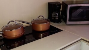 Une cuisine équipée d’une cuisinière, de deux casseroles en cuivre, d’une machine à café et d’un four à micro-ondes.