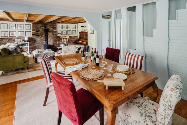Un comedor con mesa de madera, sillas rojas con estampado floral y una pared de ladrillo decorada con cuadros.