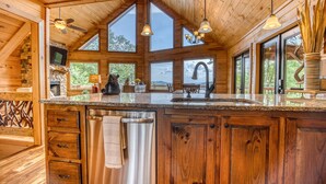 A spacious kitchen with wooden cabinetry, a large island, and a stone fireplace. - Endless Views, Secluded Cabin Hot Tub & Fireplaces (Blue Ridge)