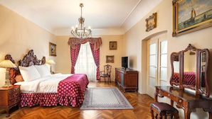 Habitación de hotel clásica con suelo de madera, una cama grande con cubrecama rojo y blanco, cómoda de madera, escritorio con espejo y candelabro.