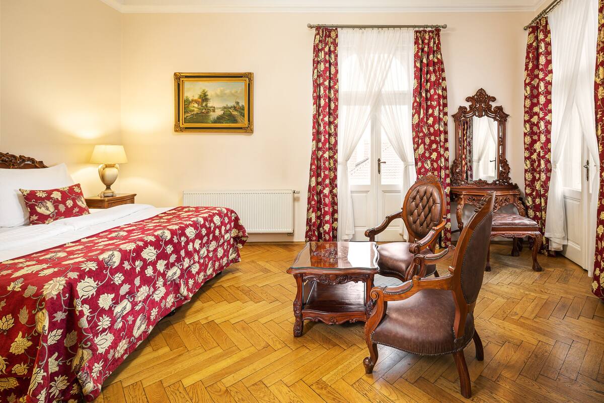 Una habitación de hotel con cama, una mesa de madera, una silla, un espejo y cortinas florales rojas.