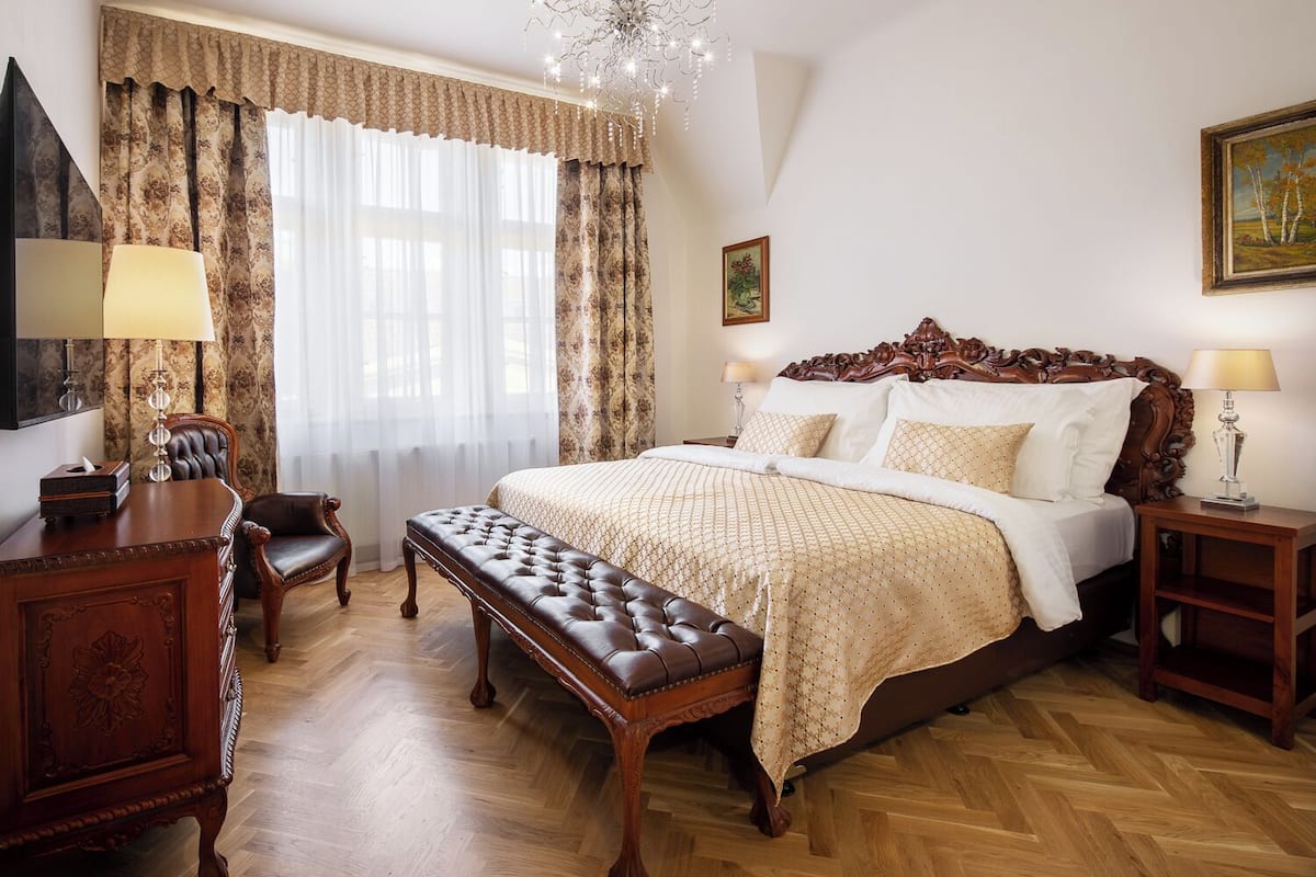 Un dormitorio con una cama grande, un escritorio de madera, un banco y una araña.