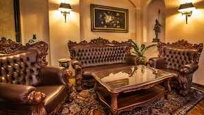 Una habitación lujosa con un sofá de cuero capitonado, muebles de madera ornamentados y una mesa de centro de vidrio.
