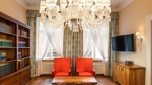Una biblioteca con estanterías, un candelabro, dos sillones rojos, una mesa de madera y un televisor en la pared.