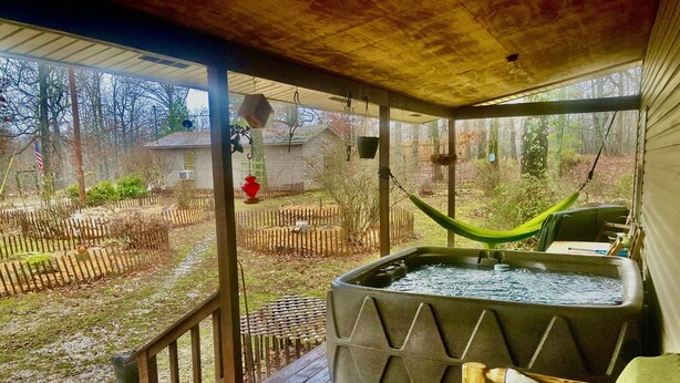 Eine überdachte Veranda mit Whirlpool, Hängematte und Holzterrasse.