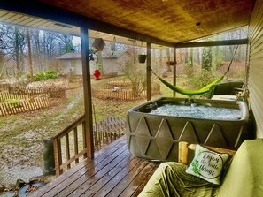 Une véranda abritée avec un jacuzzi, un hamac et une terrasse en bois.