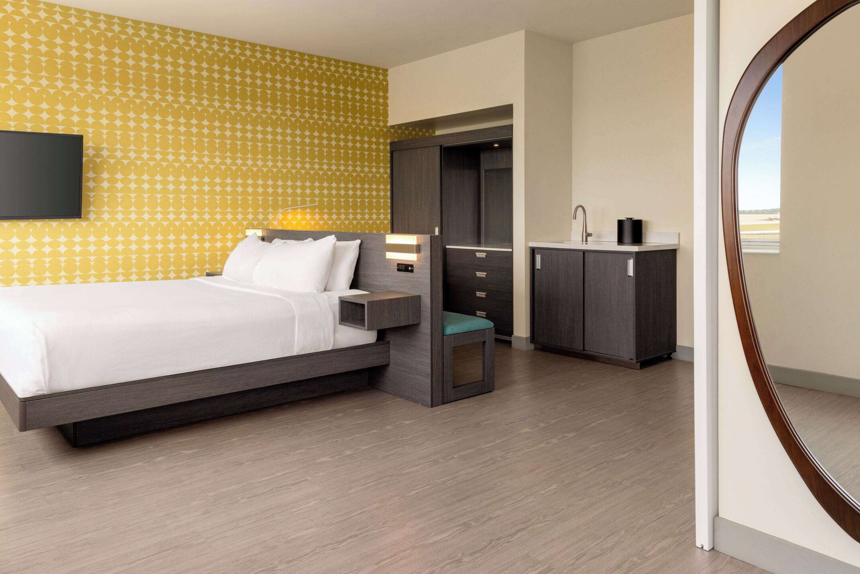 Une chambre d’hôtel moderne, dotée d’un grand lit, d’une armoire, d’une table de chevet et offrant une vue sur l’extérieur.