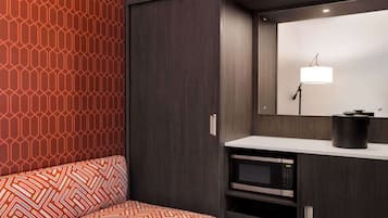 A modern room with a patterned sofa, a dark wardrobe, a built-in microwave, and a mirror with a light fixture.