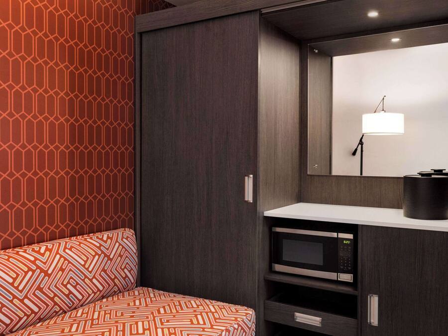 A modern room with a patterned sofa, a dark wardrobe, a built-in microwave, and a mirror with a light fixture.