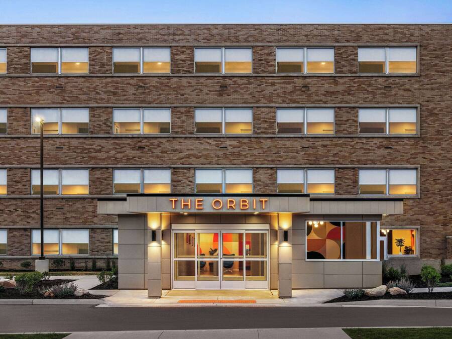 A multi-story hotel named "The Orbit" with a brick facade, large windows, and a well-lit entrance.
